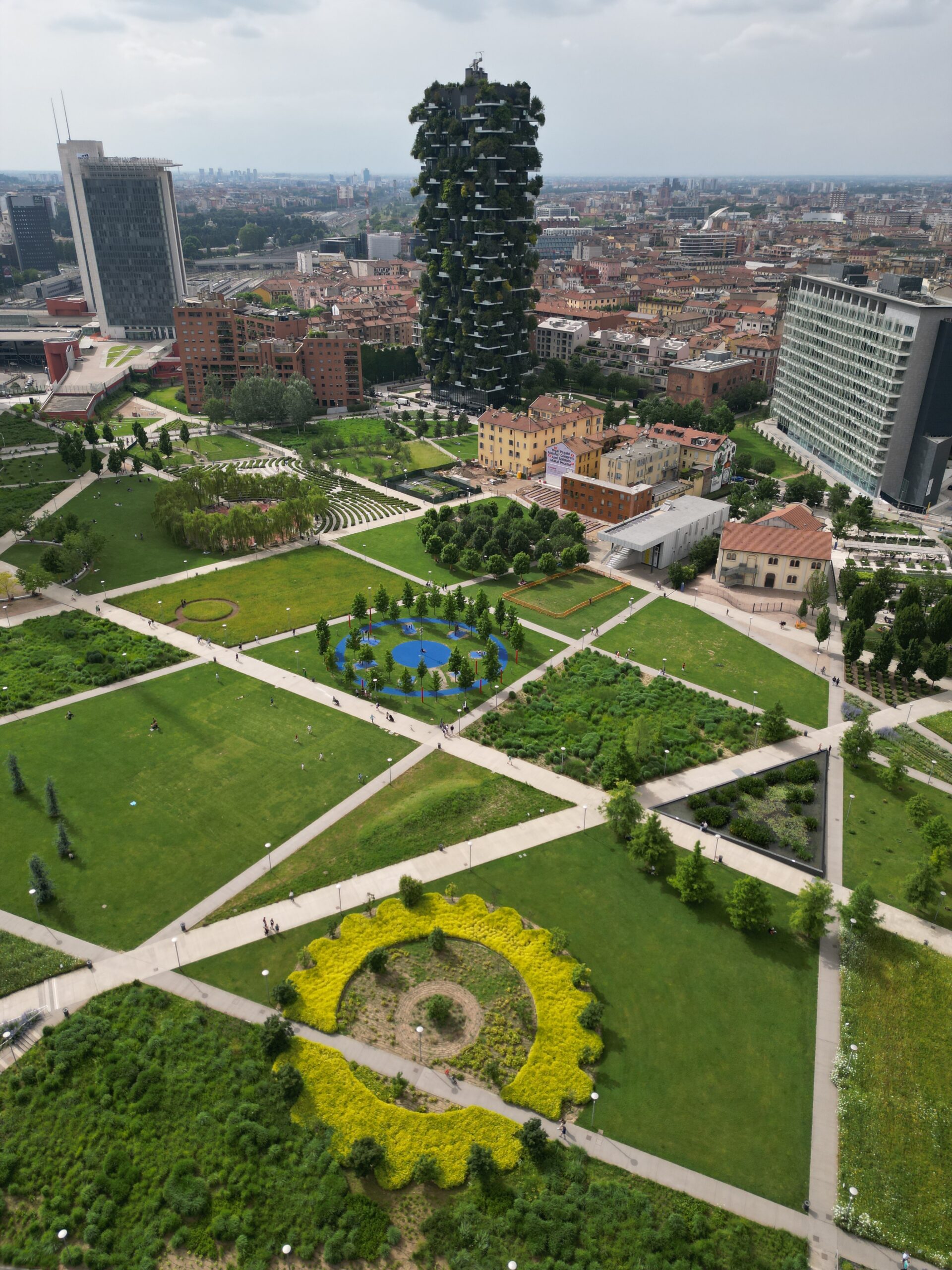 Vista dall'alto del Bosco Verticale e del parco Biblioteca degli Alberi, con l'installazione floreale gialla.