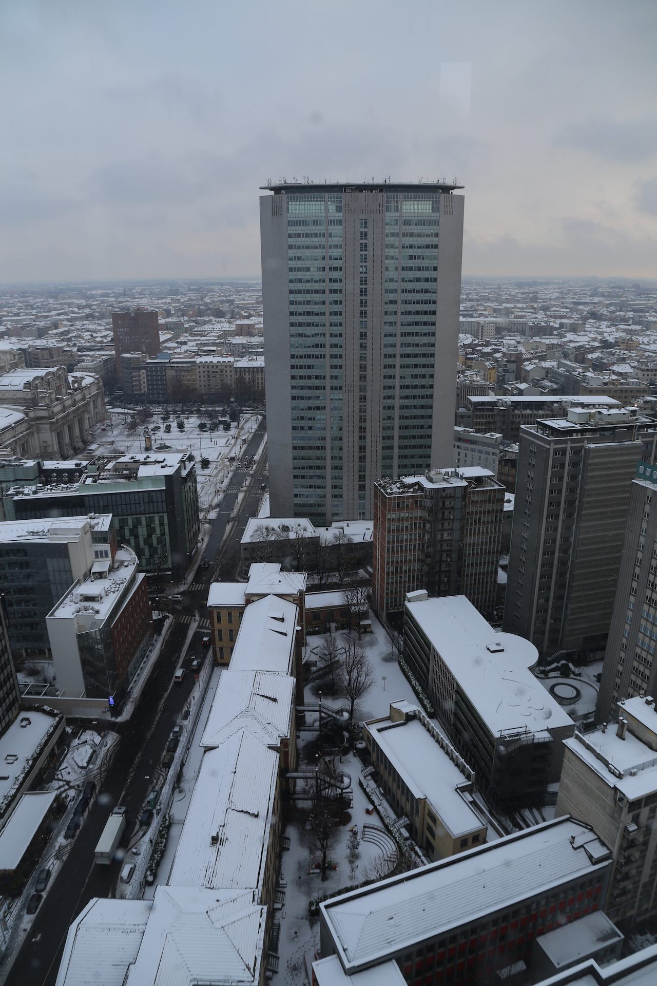 Vista verticale del Pirellone sotto la neve con Stazione Centrale sullo sfondo.