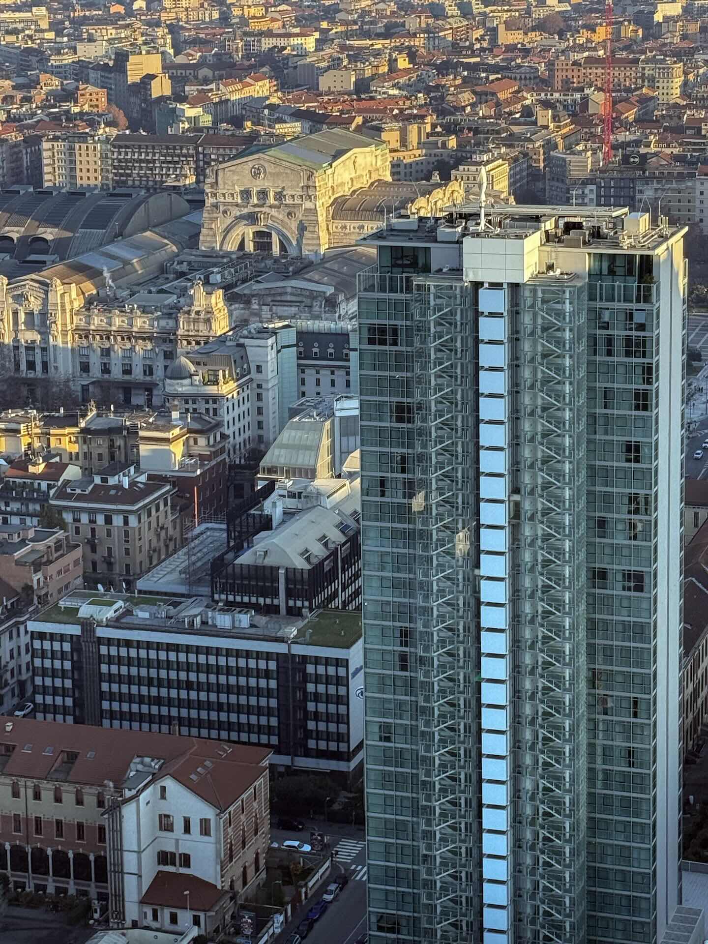La Torre Galfa al tramonto dorato, con la facciata storica della Stazione Centrale di Milano sullo sfondo.