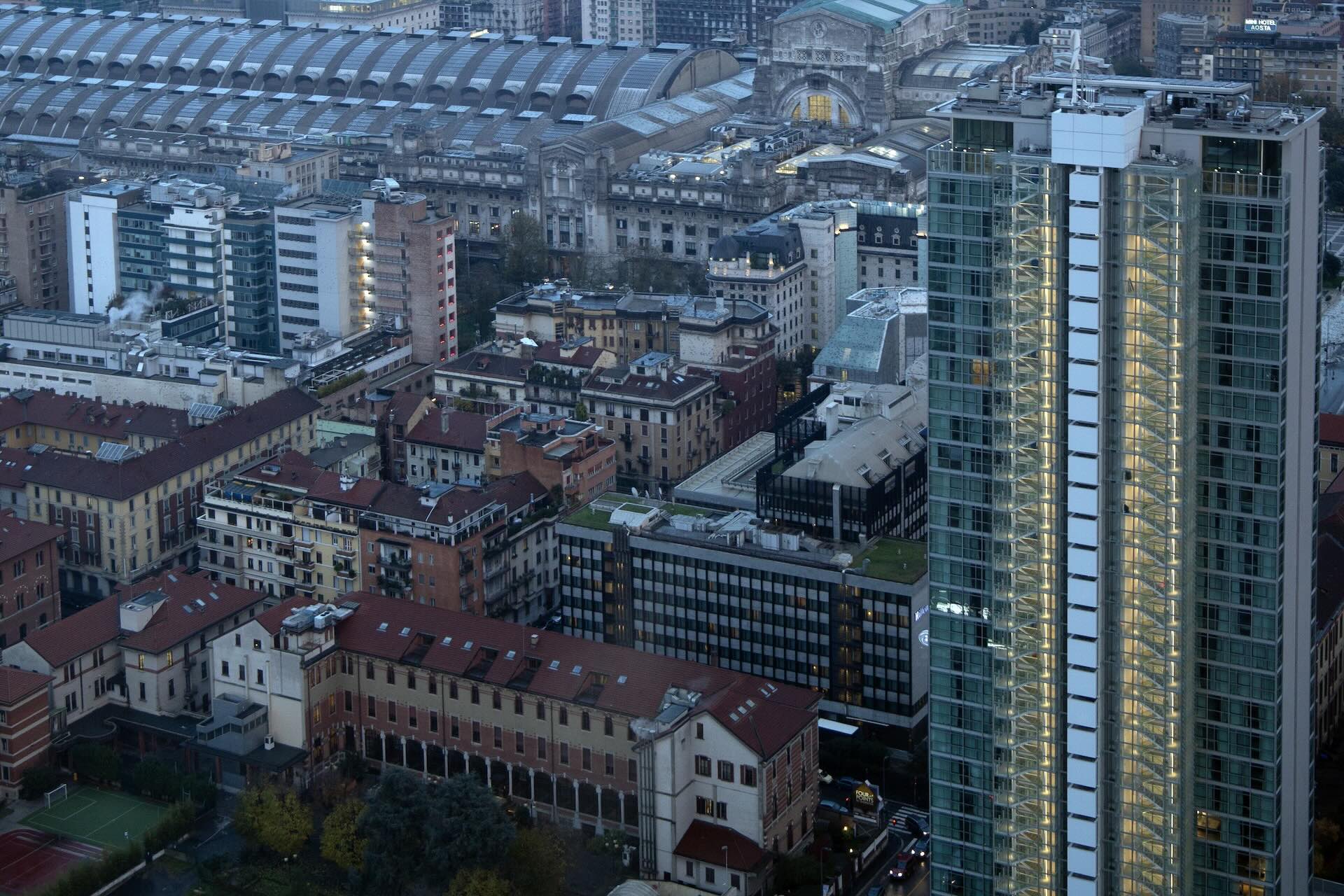 La Torre Galfa illuminata al blue hour, con la volta della Stazione Centrale sullo sfondo.