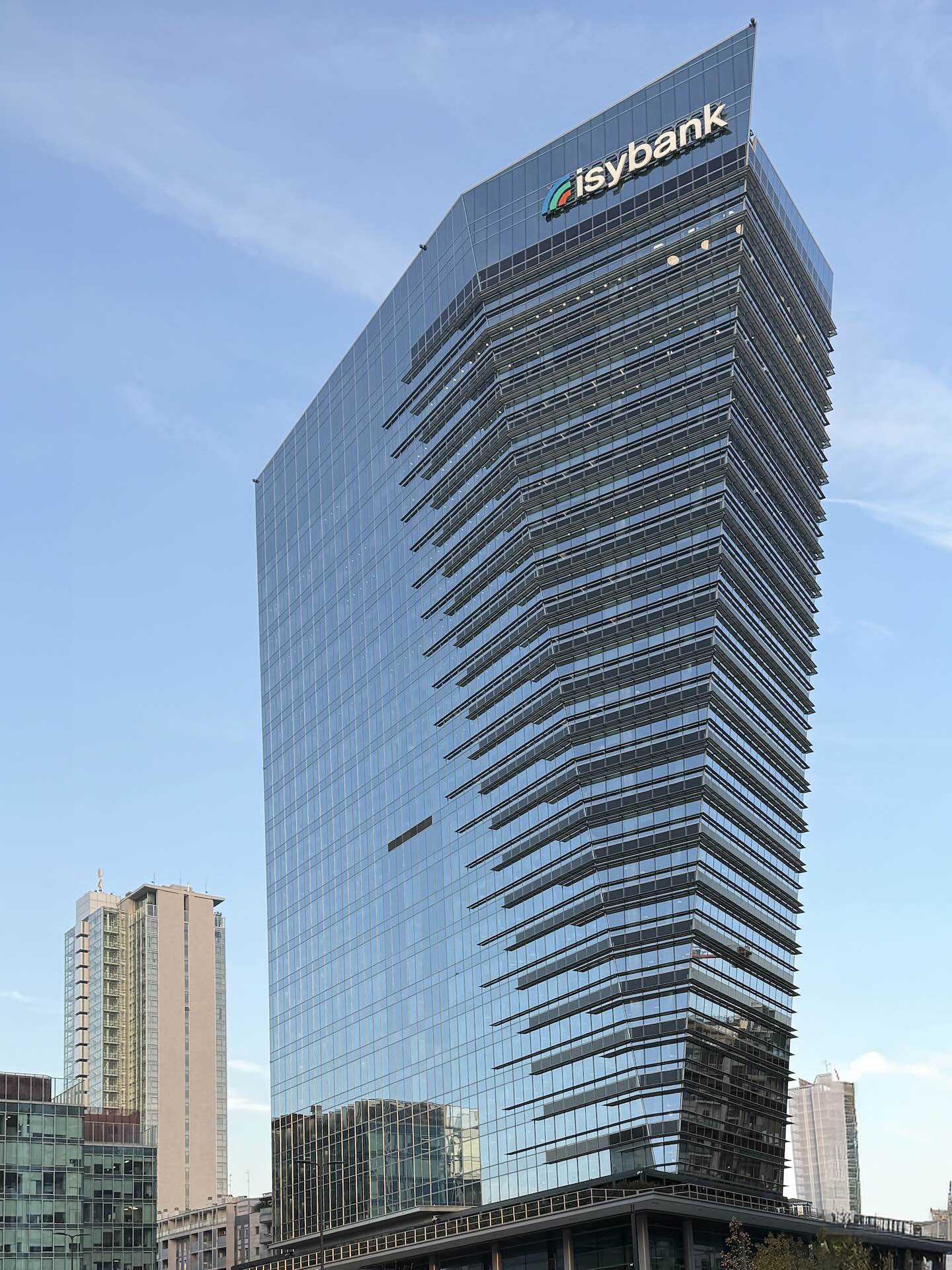 La Torre Gioia 22 ('Shard of Milan'), con il logo isybank e il profilo affilato in vetro contro il cielo blu.