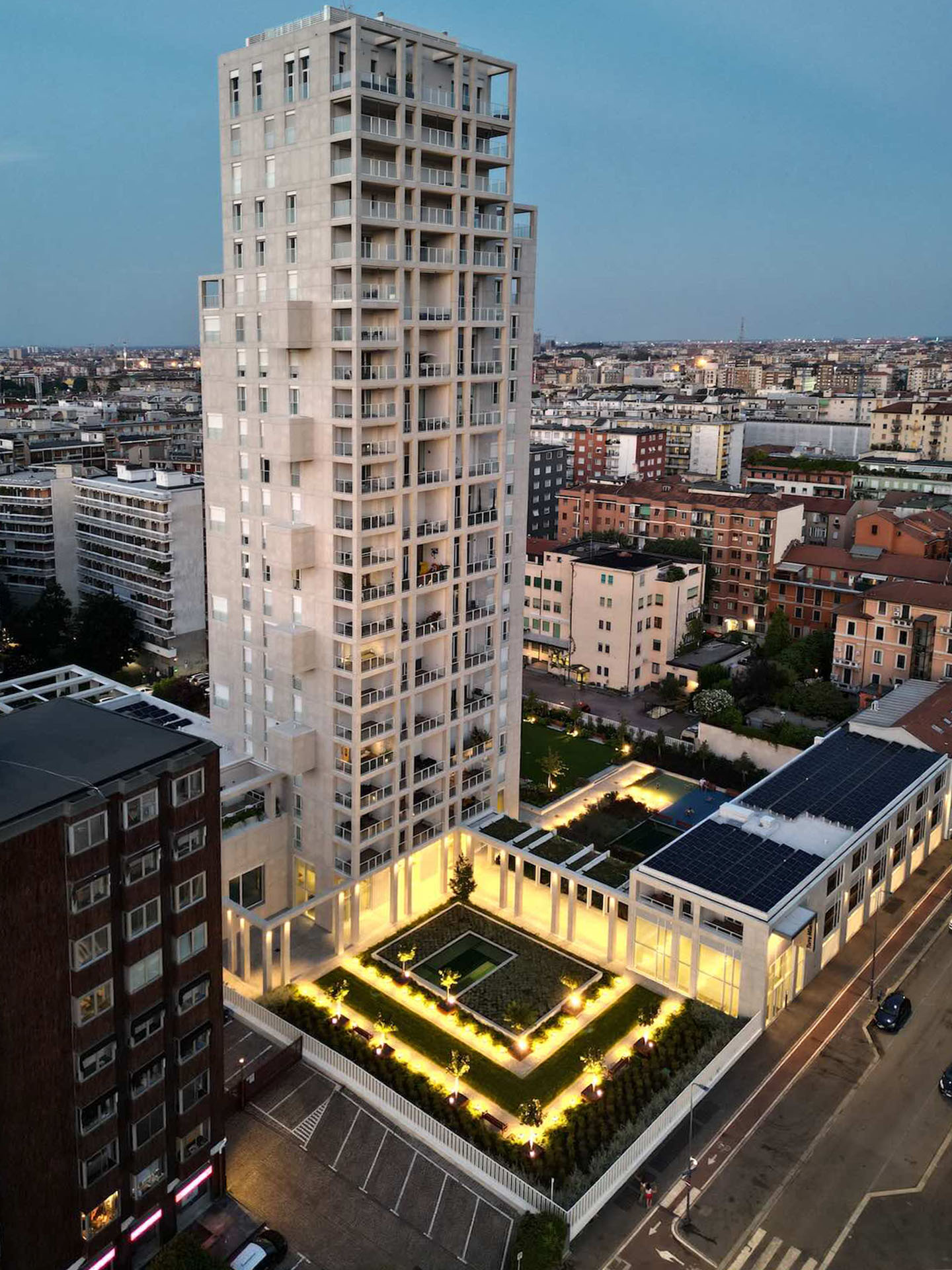 Vista aerea serale di Torre Milano, con il cortile giardino illuminato e la piscina condominiale.