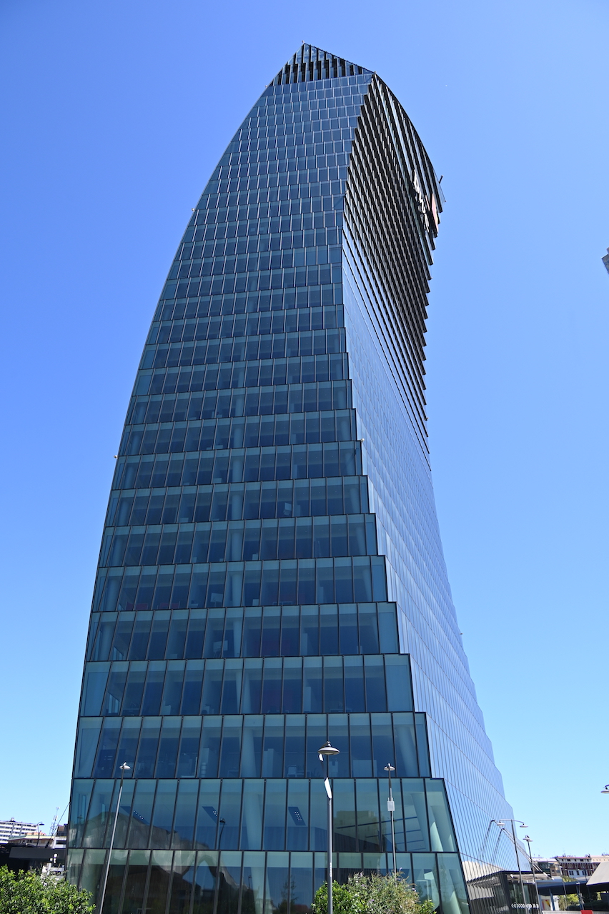 La Torre PwC contro un cielo blu terso, con il coronamento curvo in acciaio ben visibile.