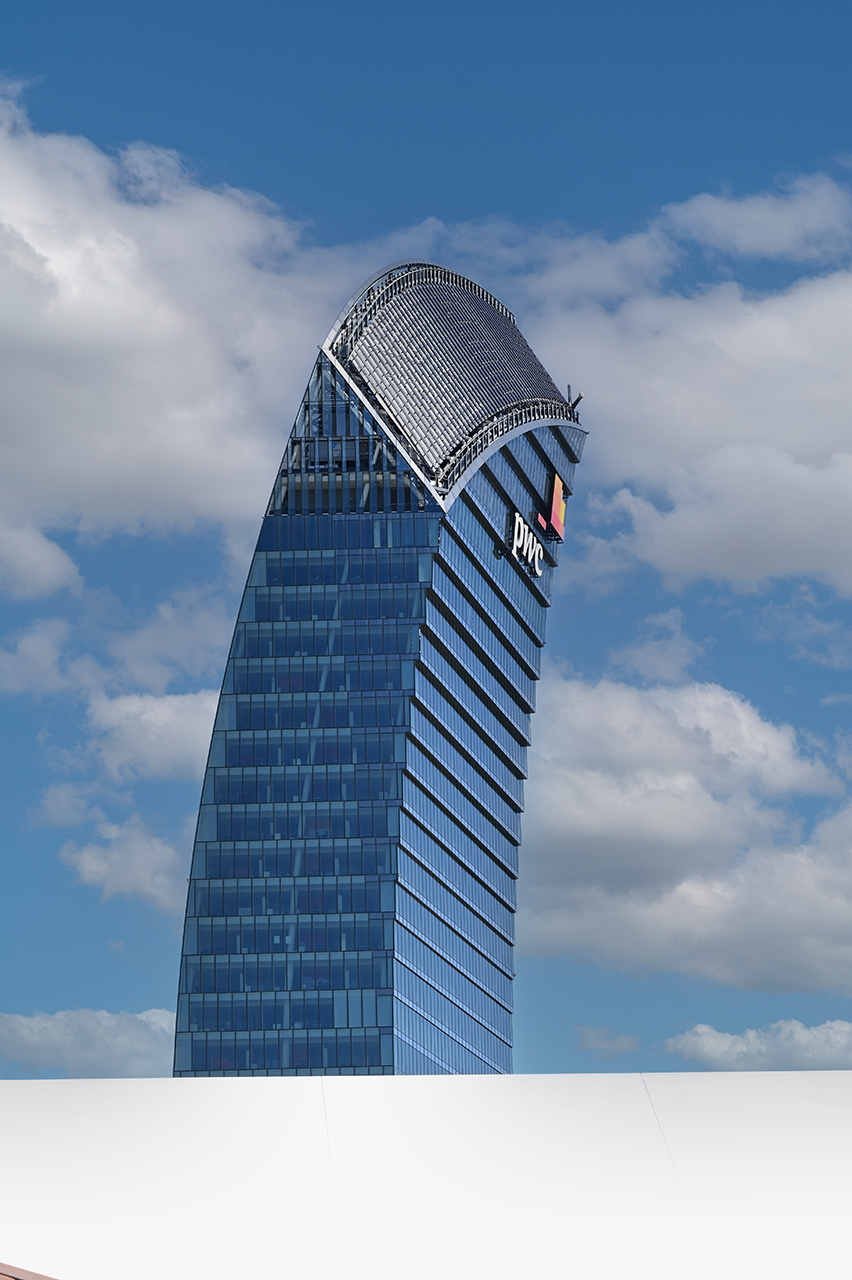 Dettaglio del coronamento in acciaio ricurvo della Torre PwC, con nuvole sullo sfondo.