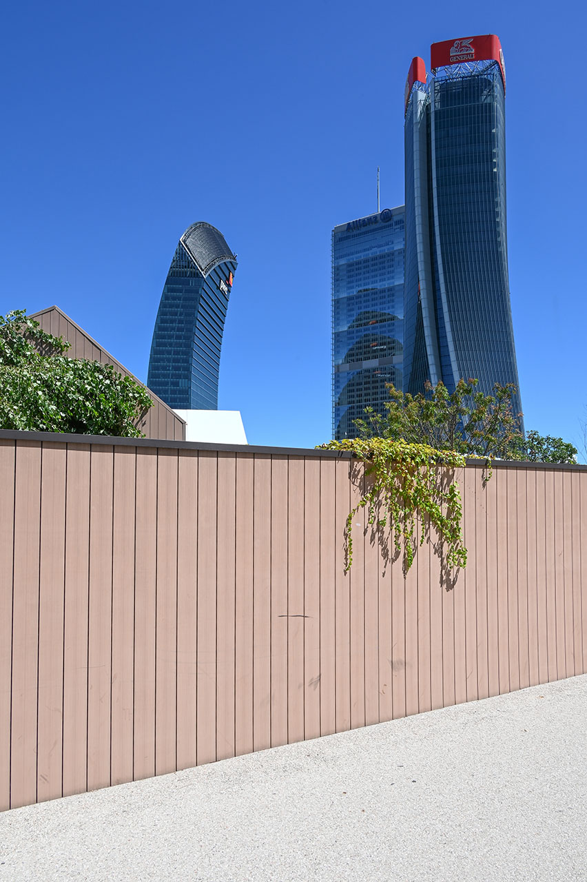 Le Tre Torri di CityLife viste da dietro una recinzione di cantiere in legno.