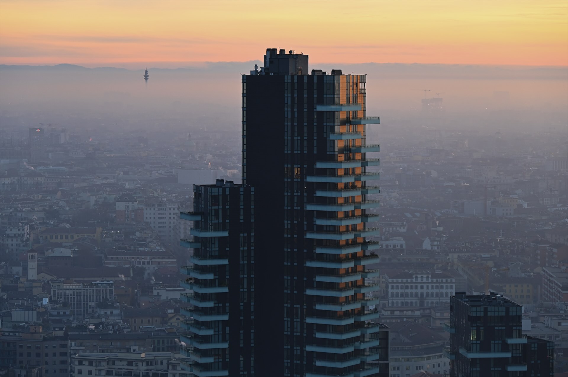 La Torre Solaria in controluce al tramonto, con la Torre Branca visibile in lontananza tra la foschia.