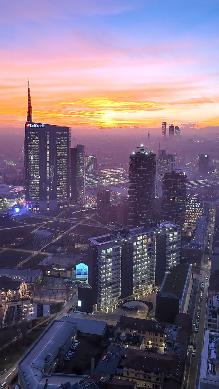 Vista dal terrazzo di Palazzo Lombardia al crepuscolo, con la Torre Unicredit illuminata e il Bosco Verticale in primo piano.