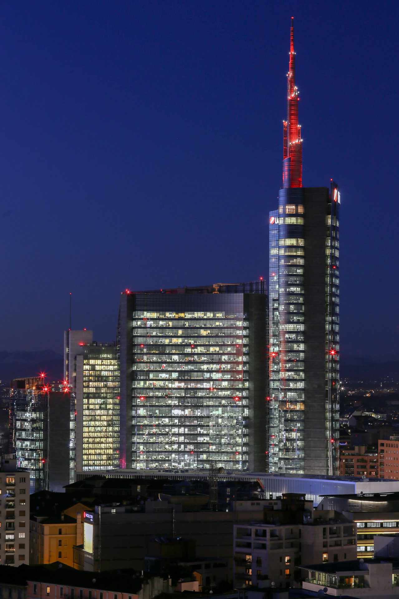 Ripresa ravvicinata della Torre Unicredit di notte, con la guglia rossa e gli uffici illuminati.