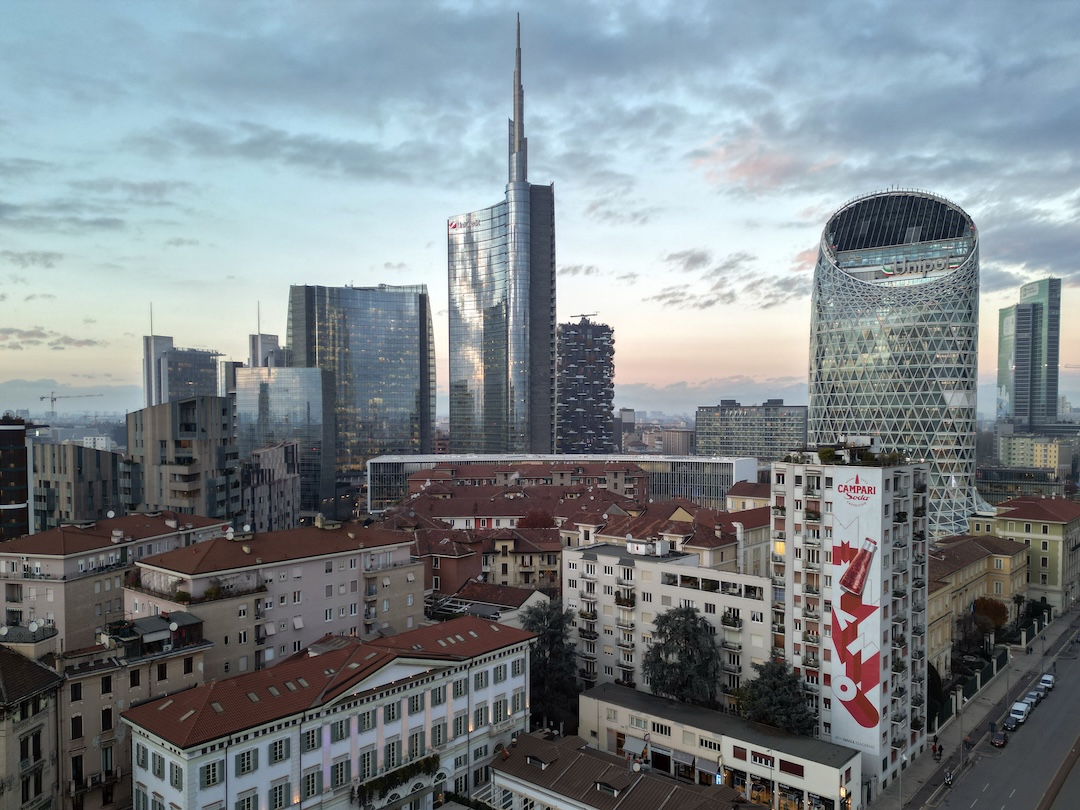 Torre Unicredit e Torre Unipol al crepuscolo, con i tetti rossi milanesi e un murale Campari in primo piano.