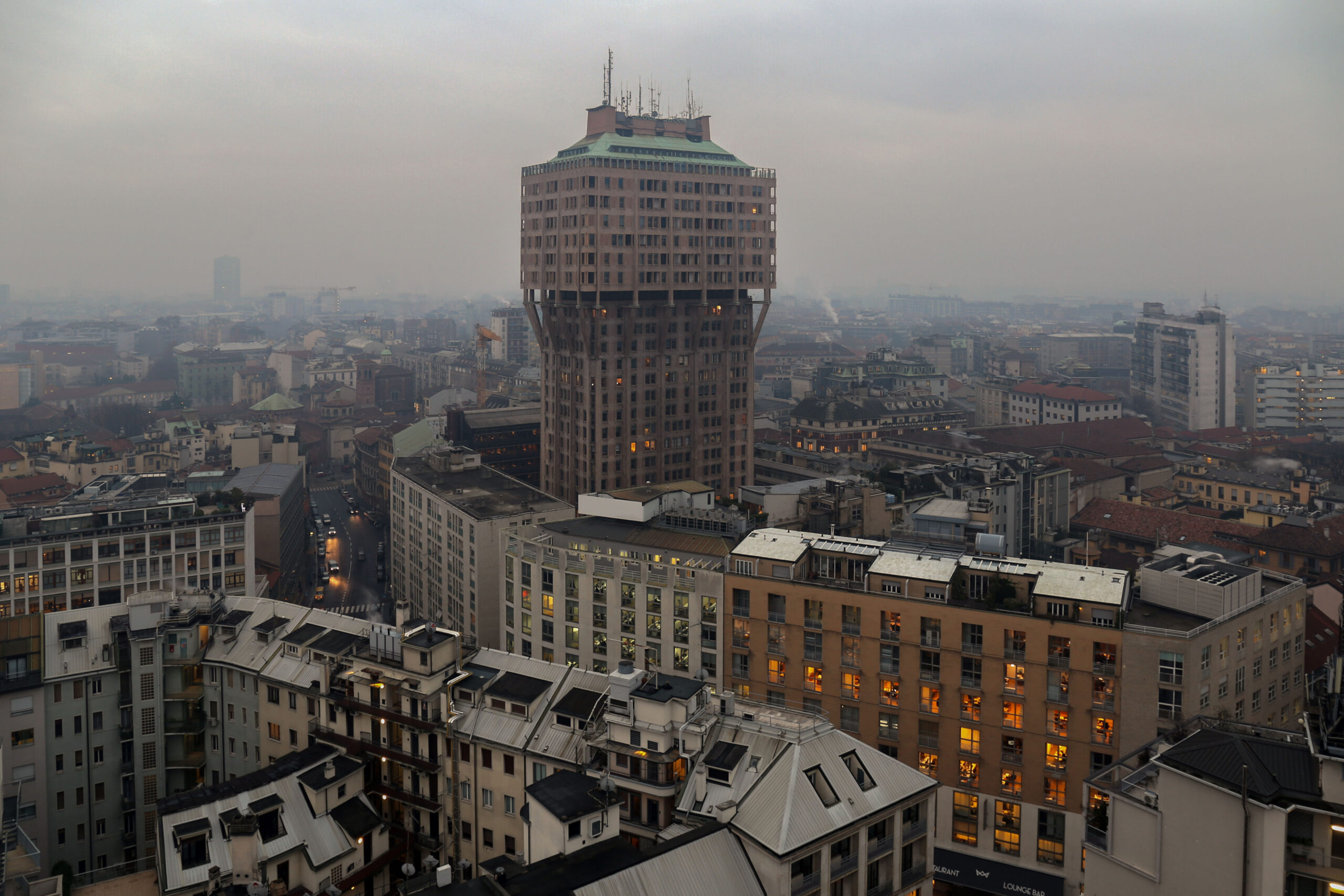 La Torre Velasca vista dall'alto in una giornata di foschia, tra i tetti del centro storico milanese.