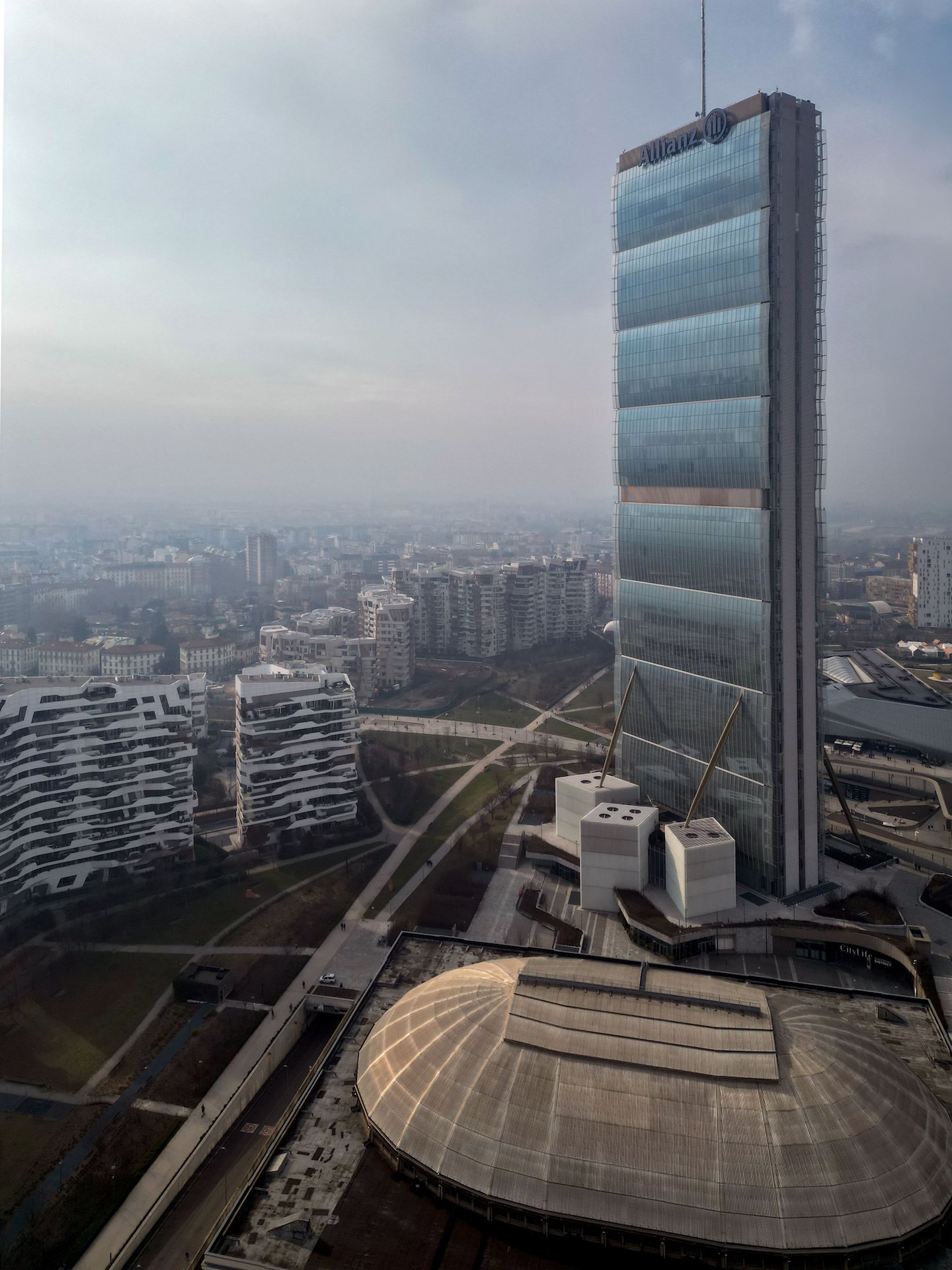 Vista aerea nebbiosa della Torre Isozaki con le residenze di CityLife e la cupola del centro commerciale in primo piano.